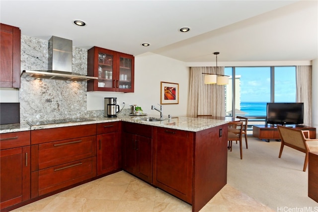 kitchen with wall chimney range hood, hanging light fixtures, light stone countertops, black electric stovetop, and sink