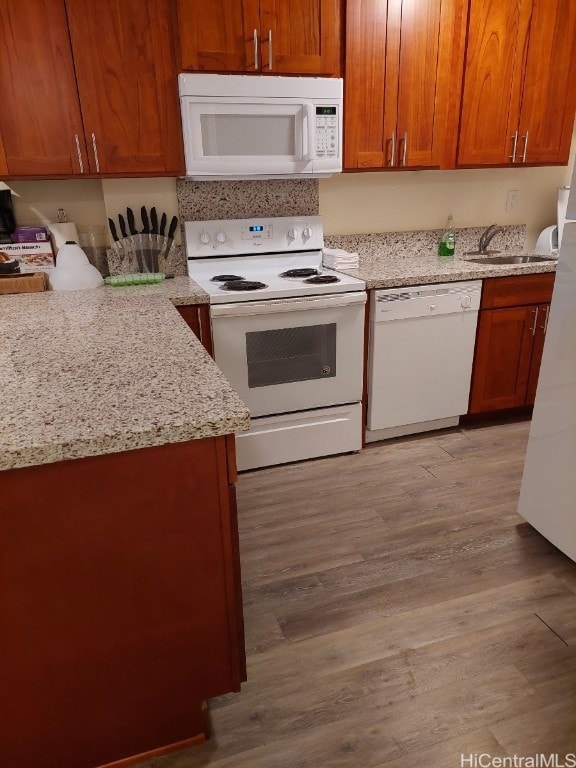 kitchen with white appliances, light stone counters, sink, and light wood-type flooring