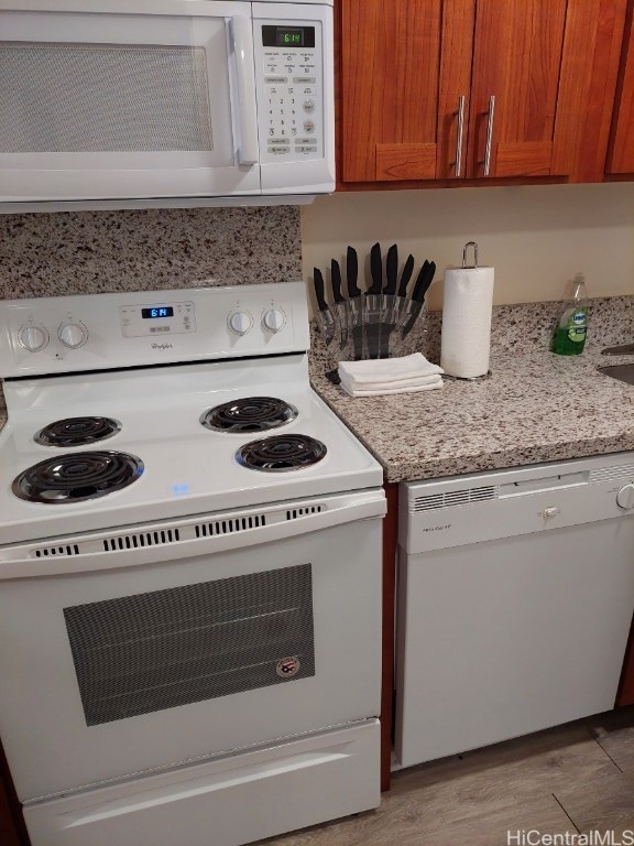 kitchen with light stone countertops, light wood-type flooring, and white appliances