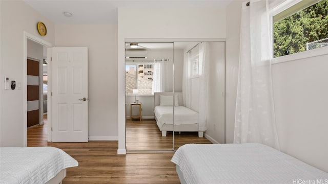 bedroom featuring dark hardwood / wood-style floors, a wall mounted air conditioner, multiple windows, and a closet