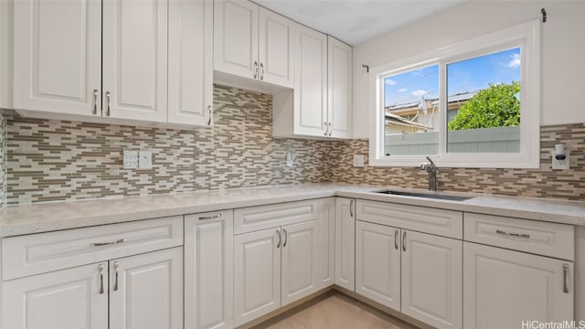 kitchen featuring light stone countertops, sink, white cabinetry, and backsplash