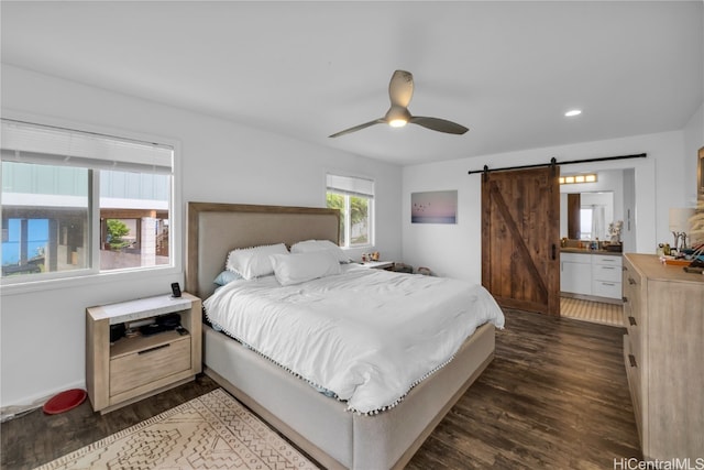 bedroom featuring ceiling fan, a barn door, dark hardwood / wood-style floors, and ensuite bathroom