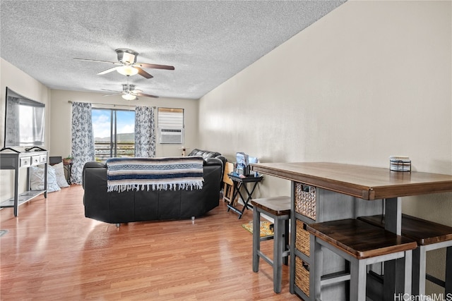 living room featuring cooling unit, a textured ceiling, light hardwood / wood-style floors, and ceiling fan