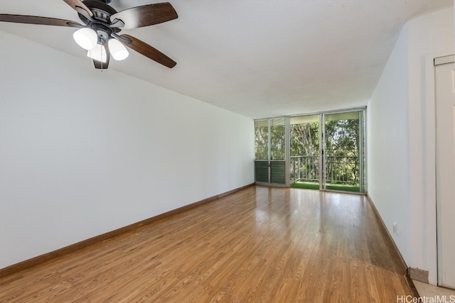 spare room featuring ceiling fan, light wood-type flooring, and a wall of windows