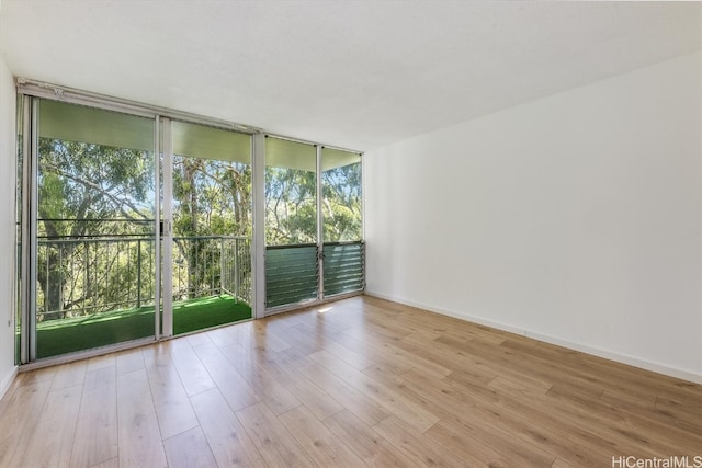 empty room featuring a wall of windows, light hardwood / wood-style flooring, and a healthy amount of sunlight