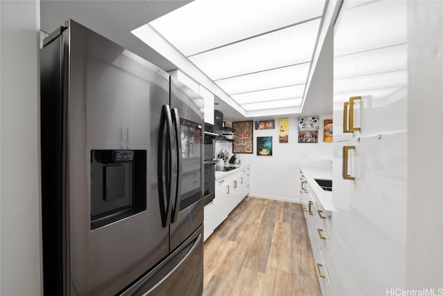 kitchen featuring sink, black electric cooktop, stainless steel fridge, white cabinetry, and light hardwood / wood-style flooring