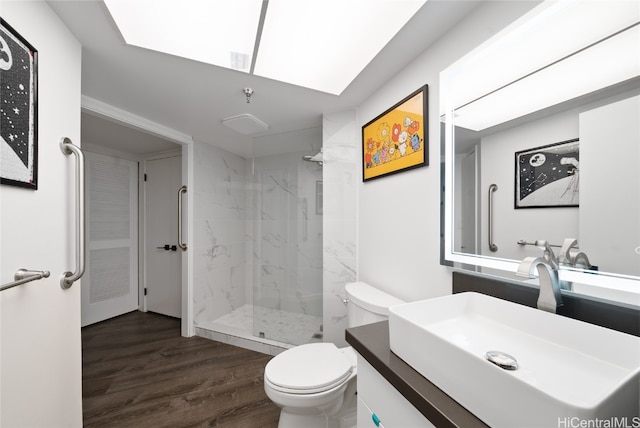 bathroom with a tile shower, a skylight, toilet, vanity, and hardwood / wood-style flooring