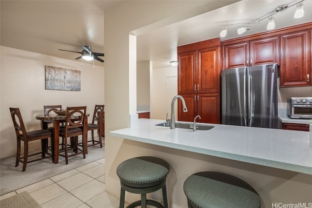 kitchen featuring a kitchen breakfast bar, kitchen peninsula, sink, light tile patterned floors, and stainless steel refrigerator