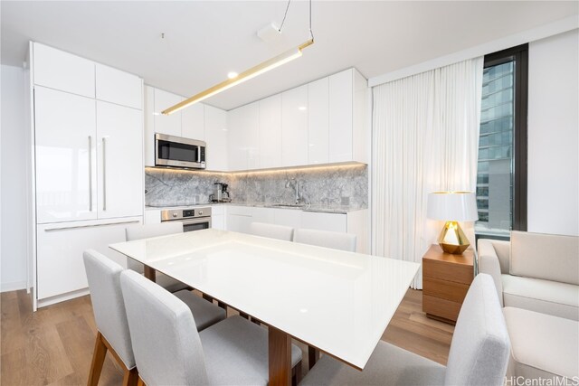 kitchen with backsplash, appliances with stainless steel finishes, light wood-type flooring, and white cabinetry