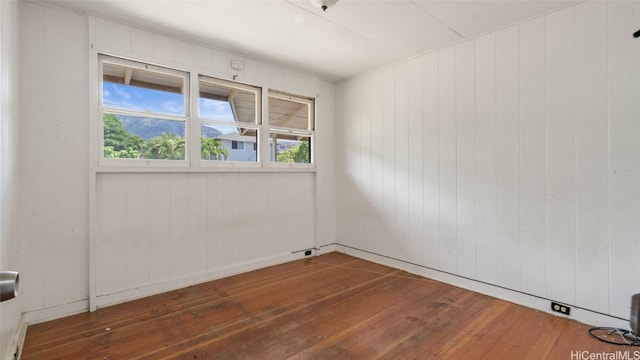 unfurnished room featuring a healthy amount of sunlight, dark hardwood / wood-style flooring, and wooden walls