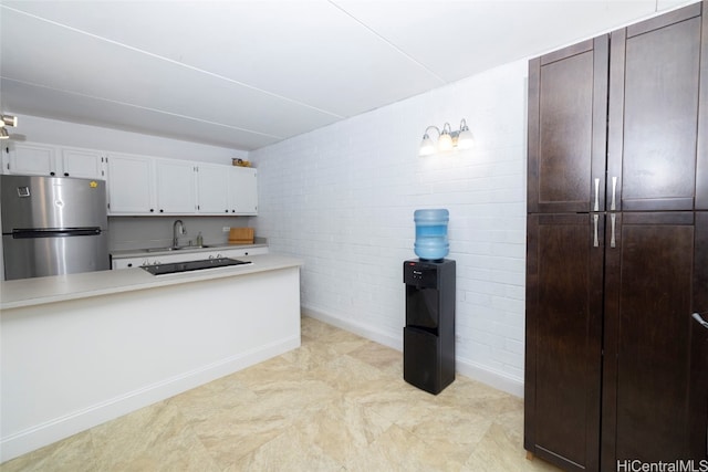 kitchen with sink, white cabinetry, pendant lighting, brick wall, and stainless steel refrigerator