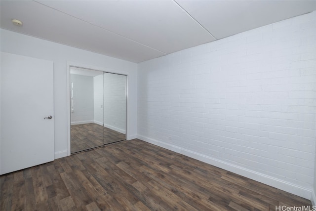 unfurnished bedroom featuring a closet, brick wall, and dark hardwood / wood-style flooring