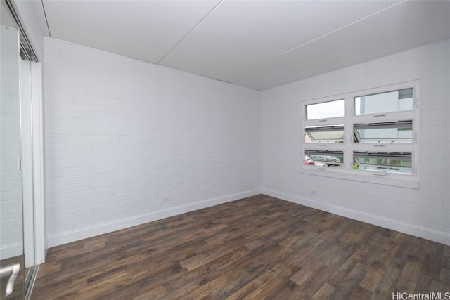 empty room with brick wall and dark hardwood / wood-style flooring