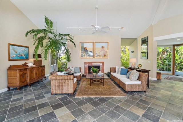 living area featuring vaulted ceiling, stone tile floors, baseboards, and ceiling fan