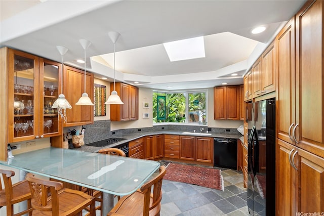 kitchen featuring a tray ceiling, glass insert cabinets, brown cabinetry, decorative light fixtures, and black appliances
