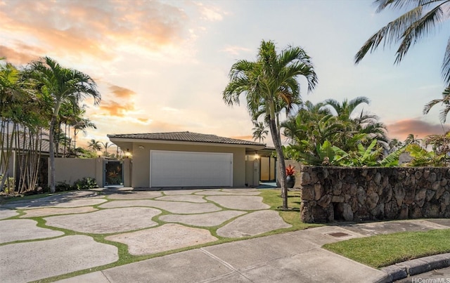 view of front facade featuring stucco siding, a tile roof, driveway, and fence