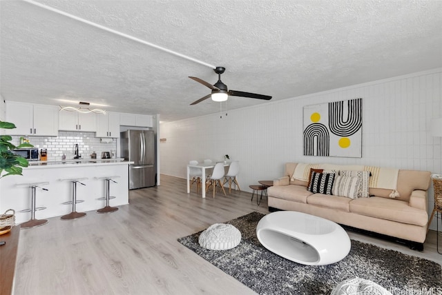 living room featuring ceiling fan, a textured ceiling, light wood-type flooring, wood walls, and sink