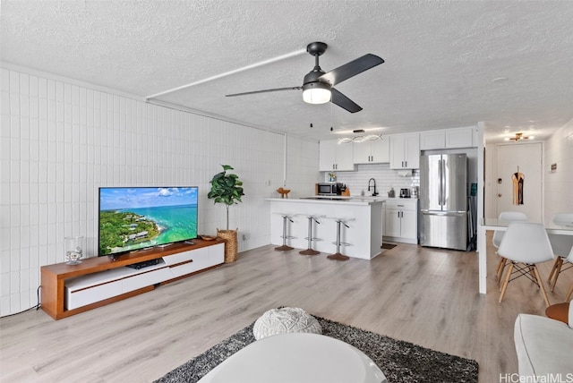 living room featuring light hardwood / wood-style floors, a textured ceiling, sink, and ceiling fan