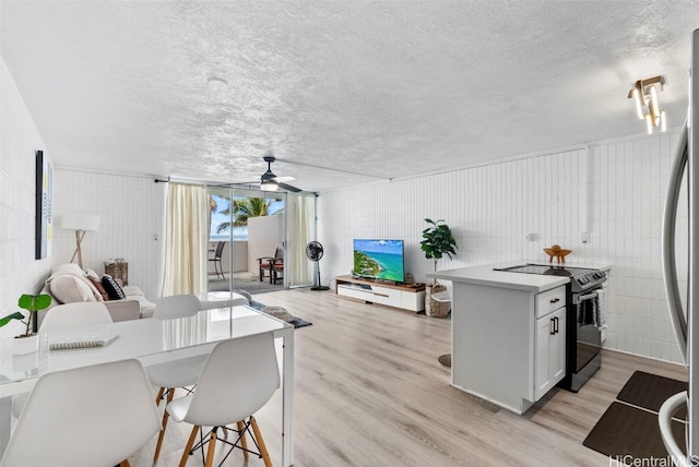 kitchen with a breakfast bar area, white cabinetry, a textured ceiling, electric stove, and light hardwood / wood-style floors