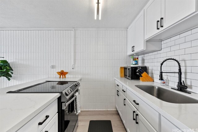 kitchen featuring white cabinets, electric range, light wood-type flooring, sink, and light stone counters