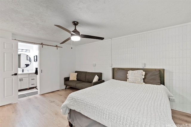 bedroom with light hardwood / wood-style flooring, a textured ceiling, connected bathroom, and ceiling fan