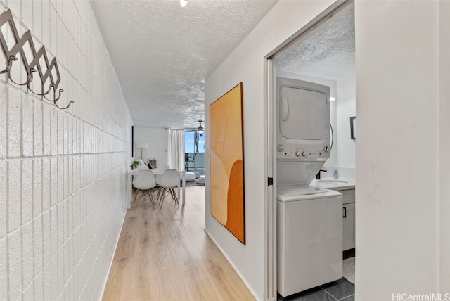 corridor featuring a textured ceiling, stacked washer and dryer, and hardwood / wood-style floors