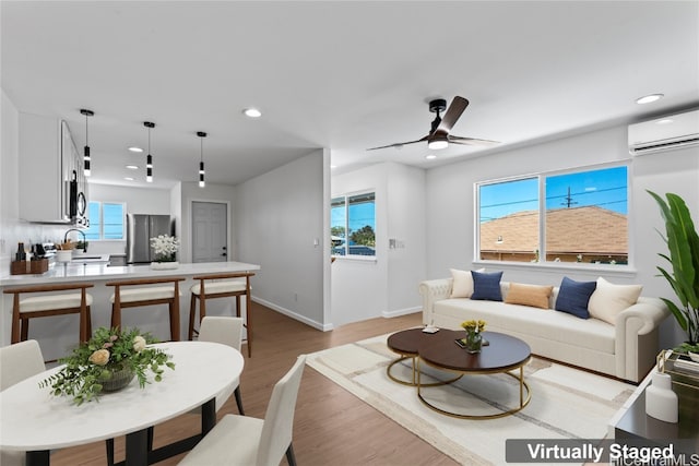 living room featuring an AC wall unit, sink, light hardwood / wood-style flooring, and ceiling fan