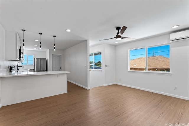 kitchen featuring an AC wall unit, hanging light fixtures, white cabinetry, hardwood / wood-style floors, and stainless steel fridge