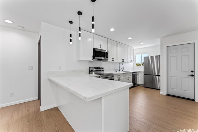 kitchen with hanging light fixtures, stainless steel appliances, kitchen peninsula, sink, and white cabinetry