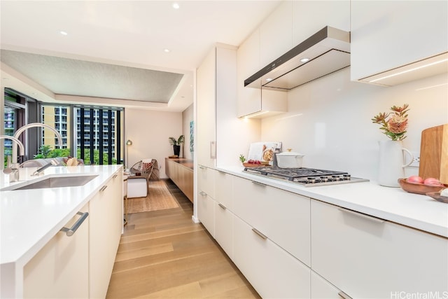 kitchen featuring sink, light wood-type flooring, stainless steel gas cooktop, white cabinetry, and ventilation hood