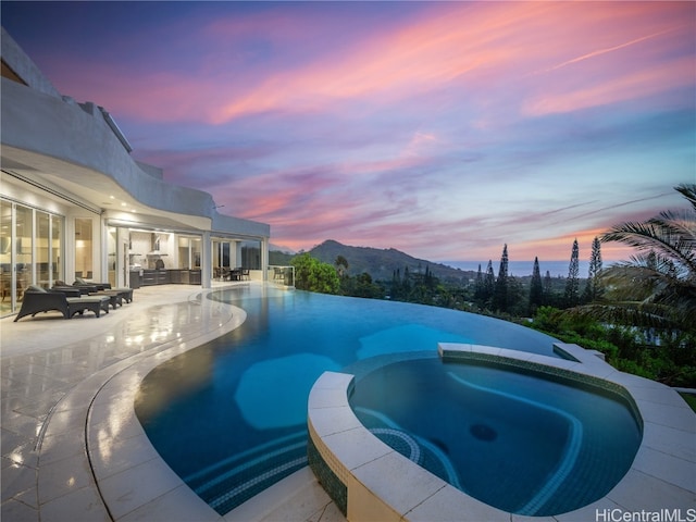 pool at dusk with a patio area, a mountain view, and an in ground hot tub