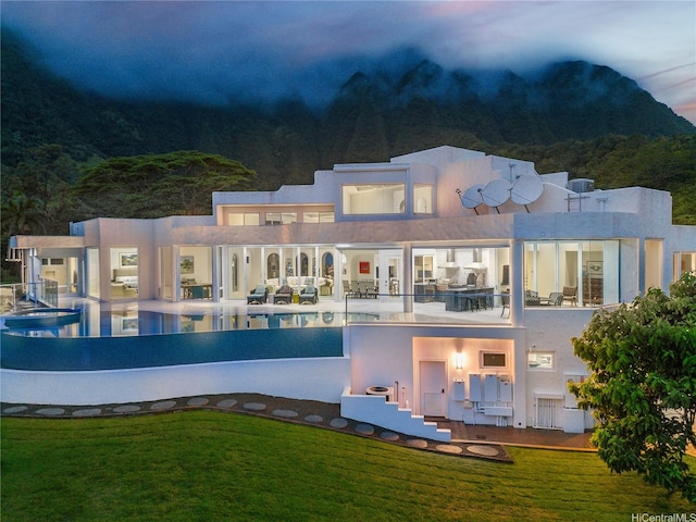 rear view of house featuring a patio, a yard, an infinity pool, and stucco siding