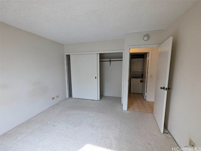 unfurnished bedroom with a closet, stacked washer / dryer, light carpet, and a textured ceiling