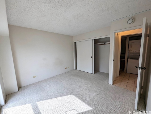 unfurnished bedroom with a closet, light carpet, a textured ceiling, and stacked washer and dryer