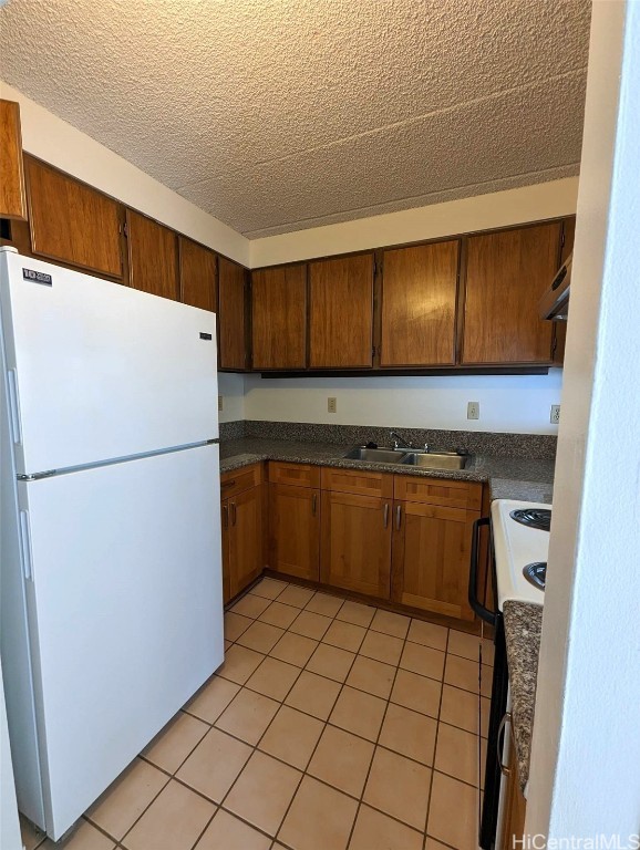 kitchen with light tile patterned floors, a textured ceiling, range hood, sink, and white appliances