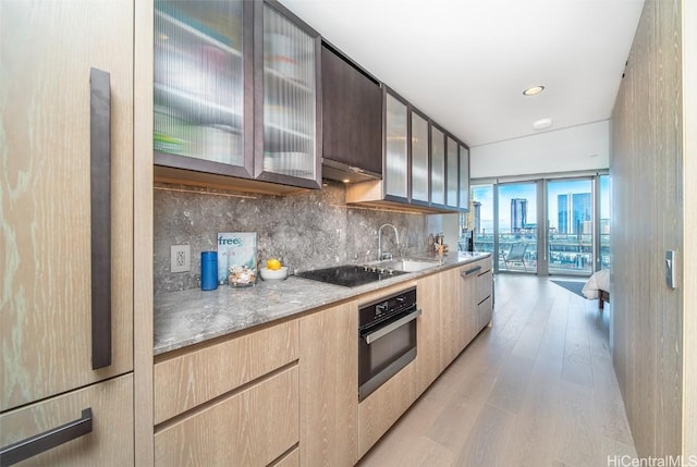 kitchen featuring a wall of windows, oven, light stone counters, light hardwood / wood-style flooring, and black electric cooktop