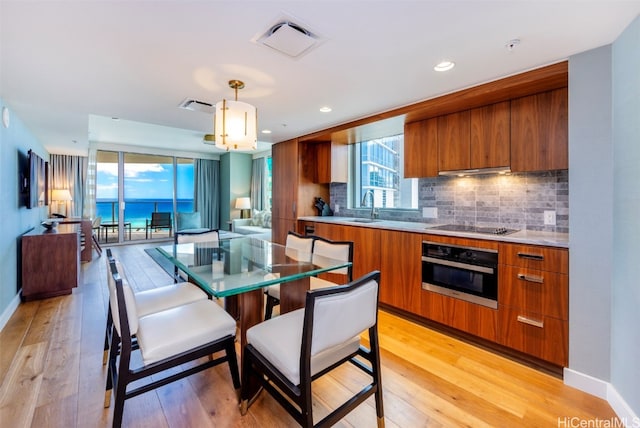 kitchen with tasteful backsplash, hanging light fixtures, stainless steel oven, light hardwood / wood-style floors, and sink