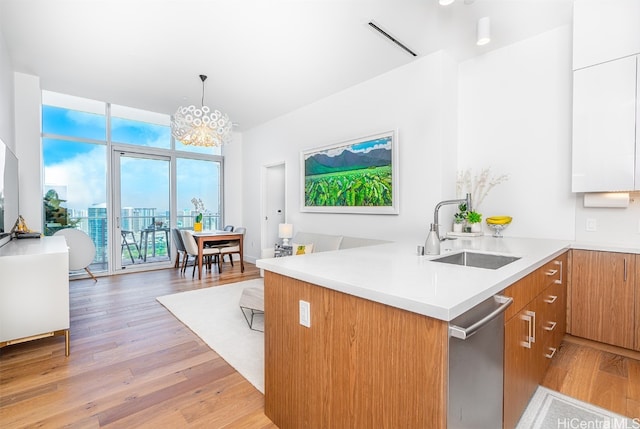 kitchen with sink, light wood-type flooring, kitchen peninsula, white cabinetry, and decorative light fixtures