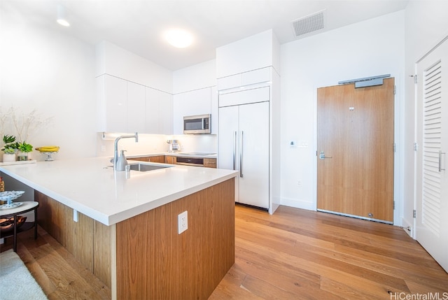 kitchen featuring sink, light wood-type flooring, kitchen peninsula, paneled fridge, and white cabinets