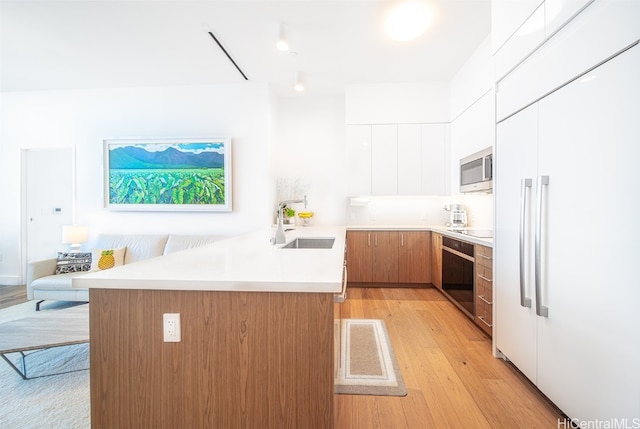 kitchen with kitchen peninsula, white cabinets, black appliances, light hardwood / wood-style floors, and sink