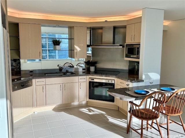 kitchen with wall chimney range hood, light brown cabinetry, black appliances, sink, and light tile patterned floors