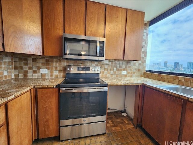 kitchen with tile countertops, appliances with stainless steel finishes, dark parquet floors, and tasteful backsplash