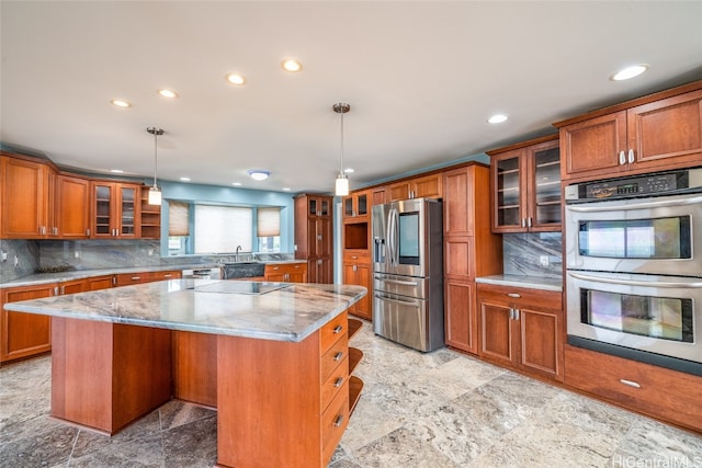 kitchen featuring tasteful backsplash, hanging light fixtures, appliances with stainless steel finishes, light stone countertops, and a center island