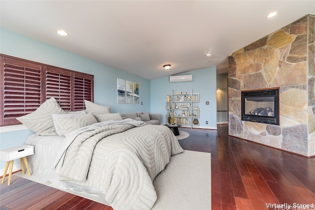 bedroom with a wall unit AC, a fireplace, vaulted ceiling, and dark hardwood / wood-style floors