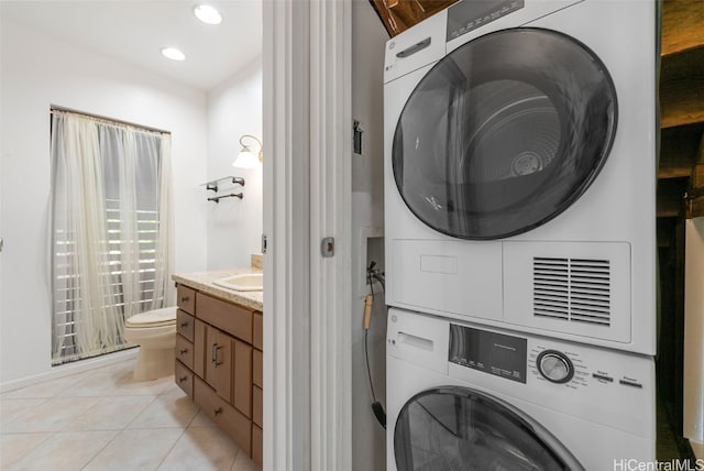 clothes washing area with sink, light tile patterned floors, and stacked washer and dryer