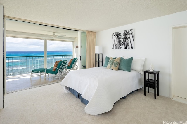 bedroom with a textured ceiling, a water view, access to outside, and carpet floors