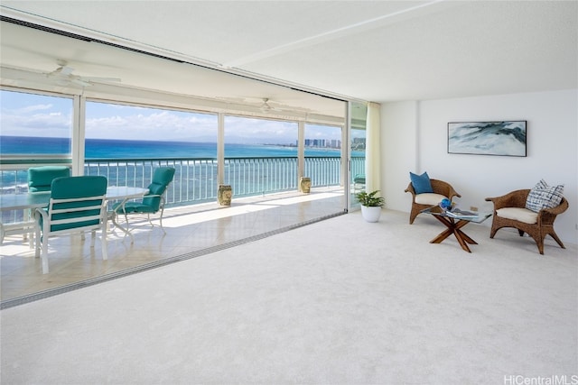 sitting room with a water view, ceiling fan, carpet, and a wall of windows