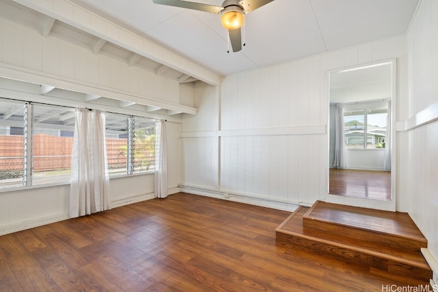 empty room with dark wood-type flooring, ceiling fan, beam ceiling, and plenty of natural light