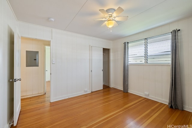 unfurnished bedroom with wooden walls, electric panel, light hardwood / wood-style floors, and ceiling fan