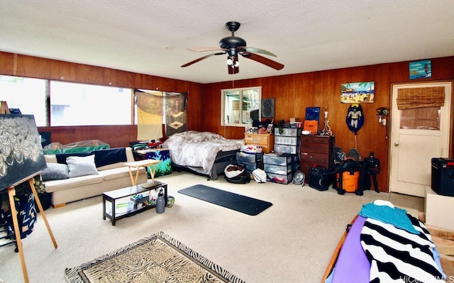 bedroom featuring wooden walls, light colored carpet, a textured ceiling, and ceiling fan